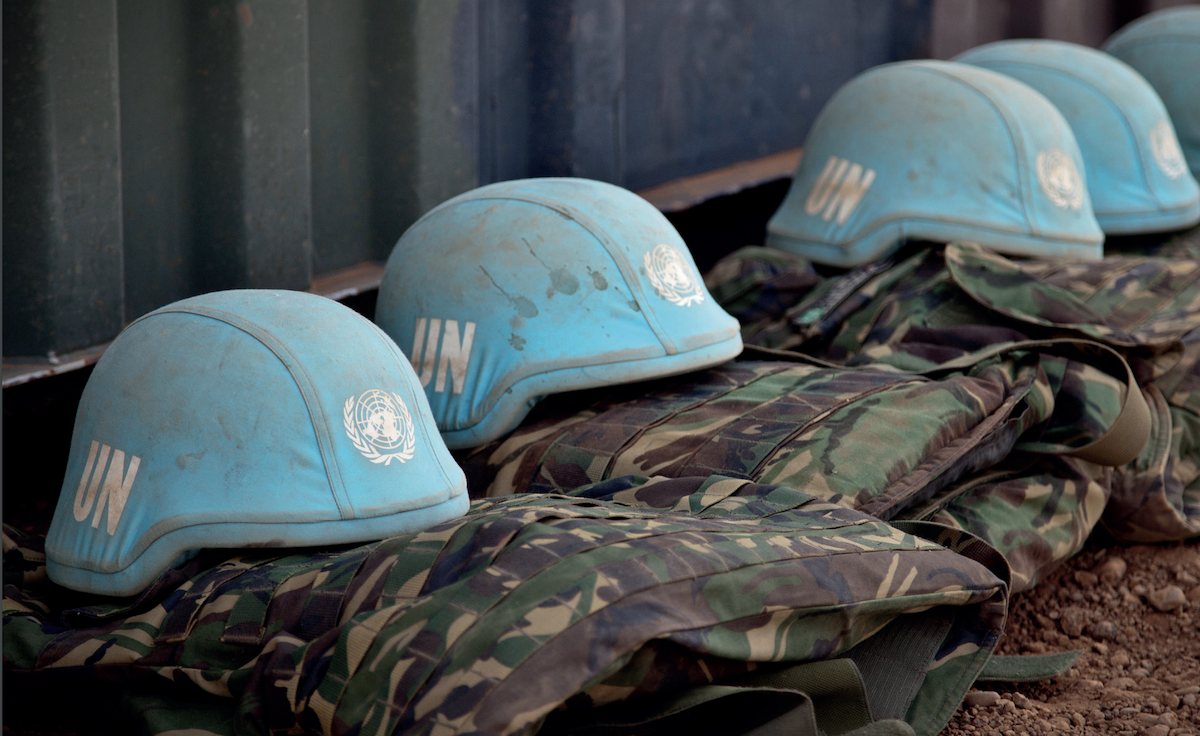 Row of UN peacekeeper helmets sitting on top of uniforms